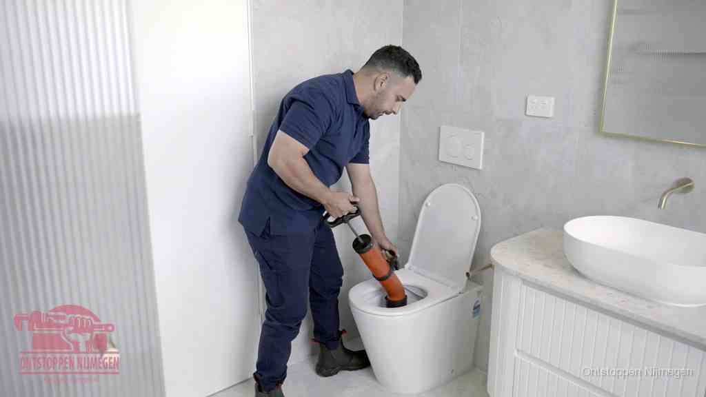 Een monteur buigt over een wandcloset en duwt met de hand een persluchtontstopper in de toiletpot om de verstopping handmatig los te maken in Nijmegen