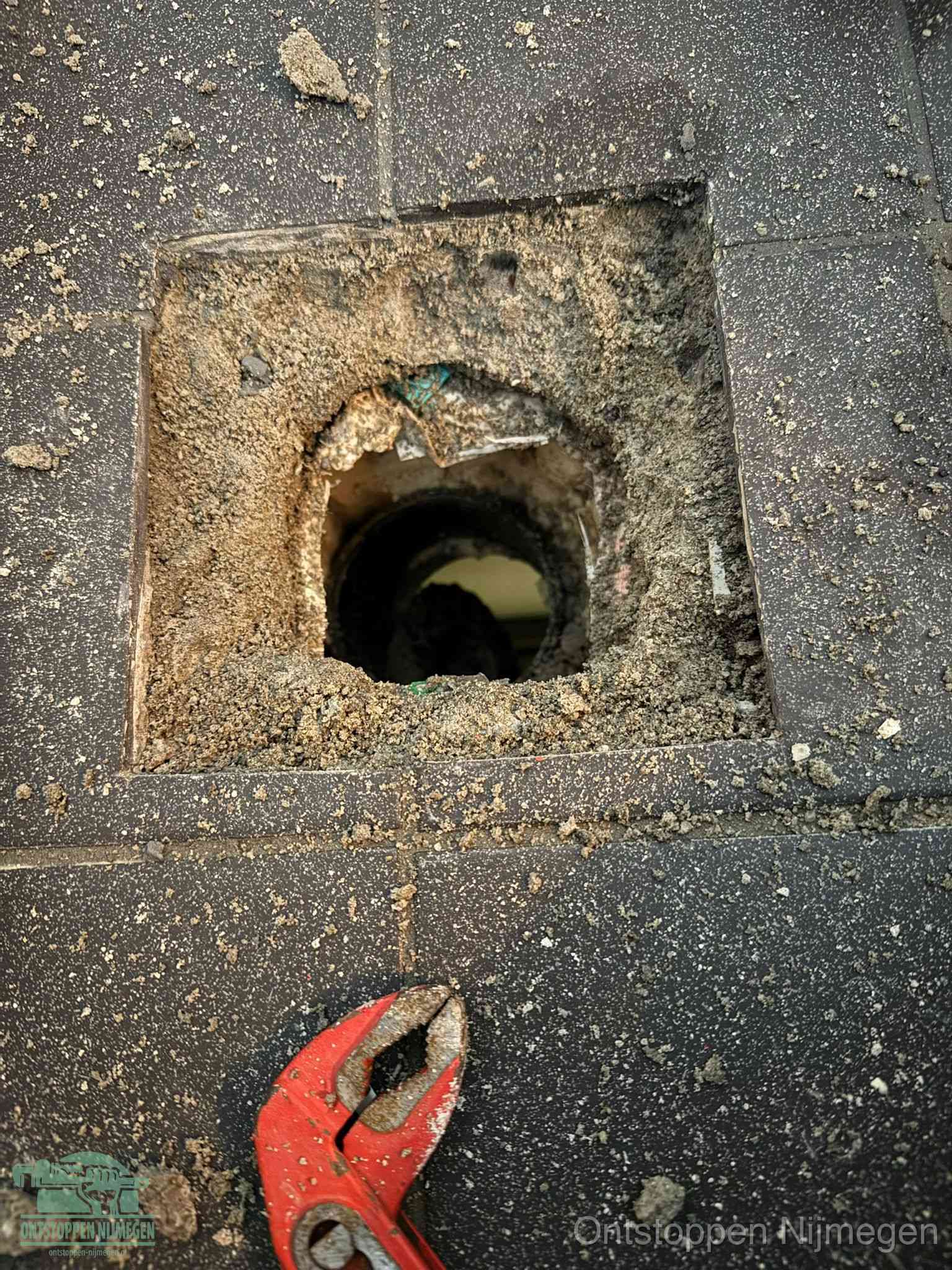 Een geopend rioolputje in een betontegelvloer met losgemaakt rooster en een zichtbare ronde afvoerbuis, het achterhalen waar de afvoerverstopping zit in Nijmegen