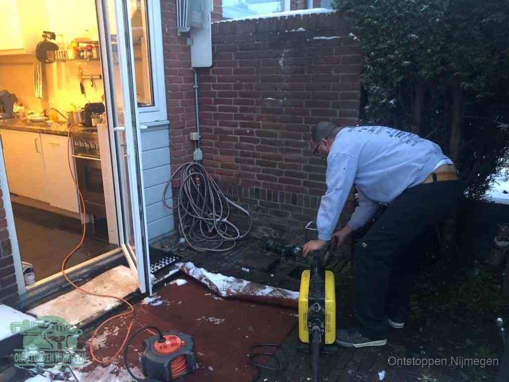 Een monteur werkt buiten bij een open riool-/grondput met een elektrische ontstoppingsmachine om een verborgen afvoerprobleem op te sporen in Nijmegen