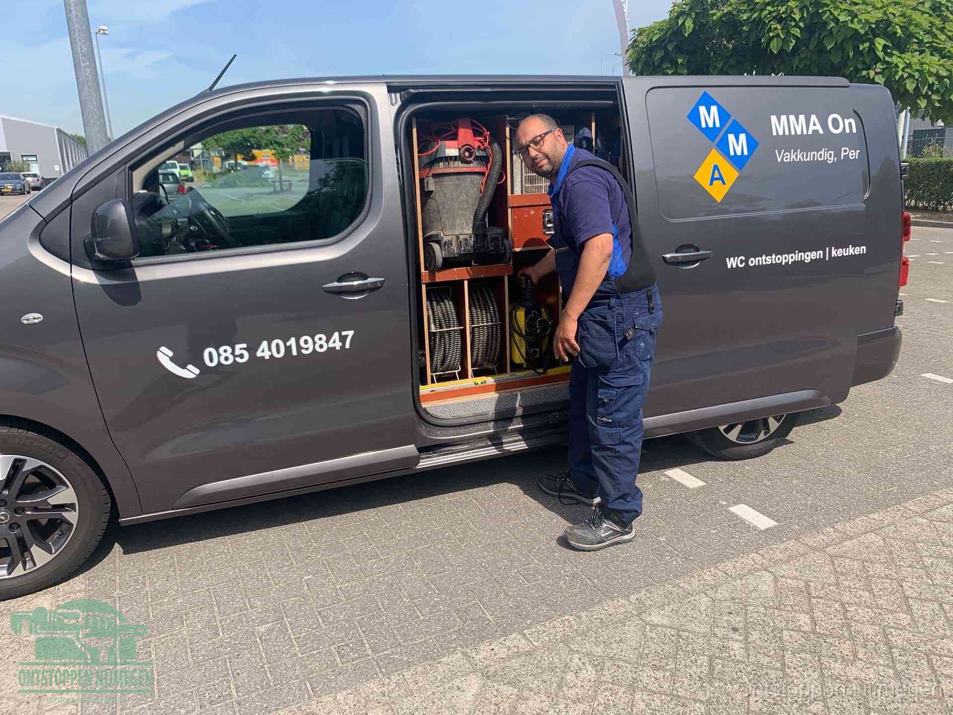 Een monteur bij de open schuifdeur van zijn bedrijfsbus op een parkeerplaats, klaar om de oorzaak van terugkerende afvoerverstoppingen aan te pakken in Nijmegen