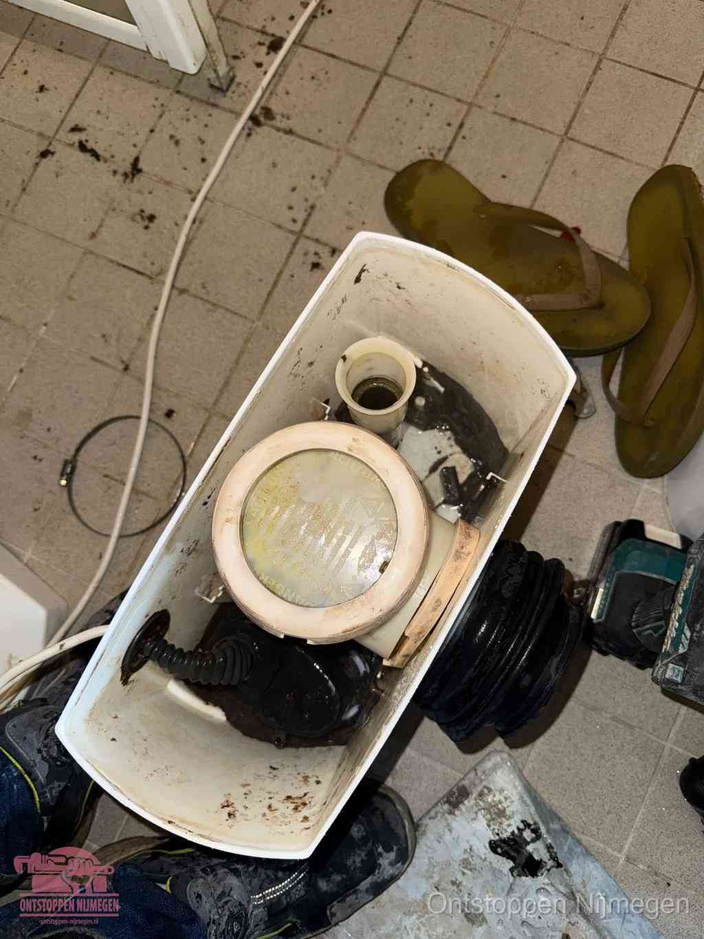Een gedemonteerde toiletpot op de vloer met ontstoppingsveer en gereedschap ernaast, het verwijderen van een vastzittend voorwerp uit de wc in Nijmegen