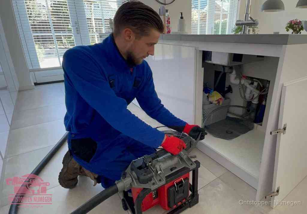 Een monteur voert een professionele elektrische ontstoppingsmachine in de afvoer onder de spoelbak tijdens het gootsteen ontstoppen in Nijmegen