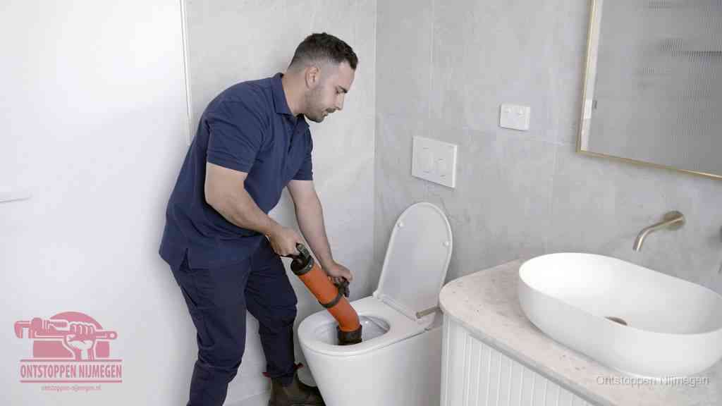 Een man gebruikt een handmatige luchtdruk-ontstopper in een modern betegeld toilet om zelf de wc te ontstoppen in Nijmegen